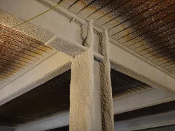 Cementitious vermiculite spray applied to a steel beam and column beneath a metal deck